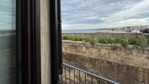 Une vue depuis une fenêtre donnant sur un paysage côtier, avec un mur de pierre et une étendue d’eau au loin.
