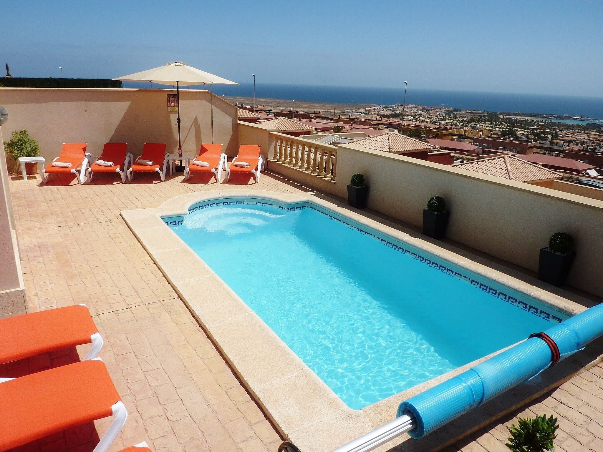 Pool på taget med orange liggestole og udsigt over byen og havet.