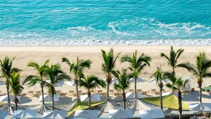 Une plage avec des parasols blancs et des palmiers.