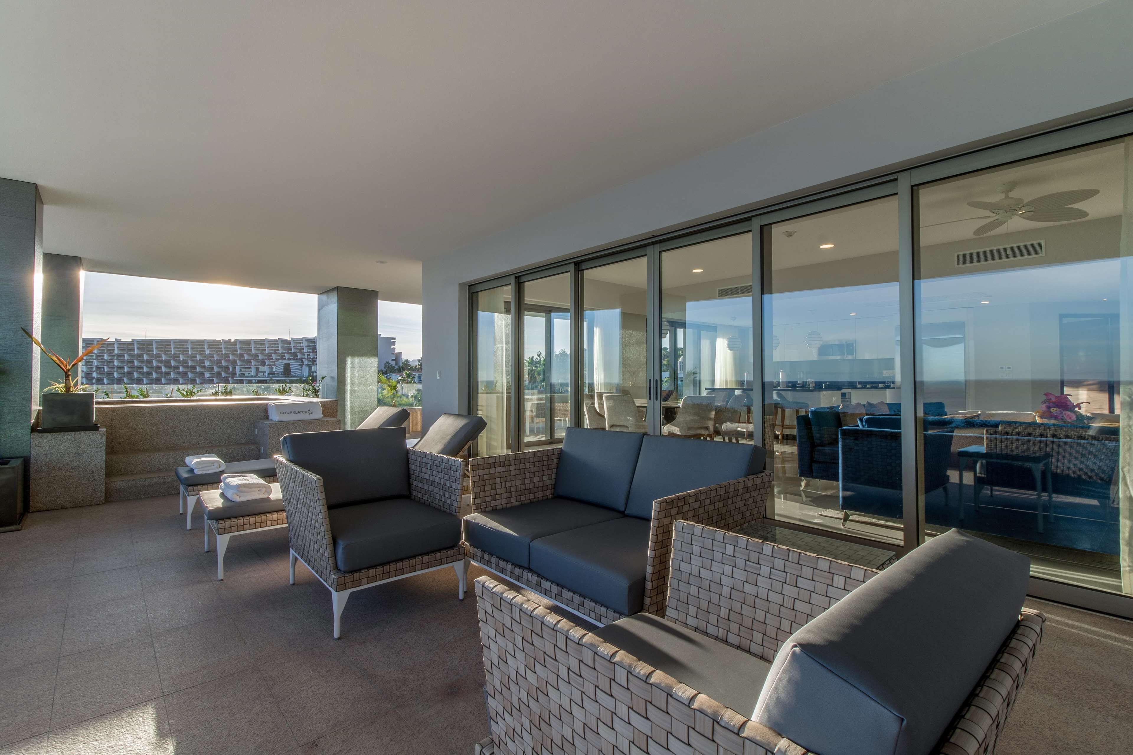Un espace de détente ext érieur moderne, avec des meubles en osier, un mur de verre et une vue sur le paysage urbain.
