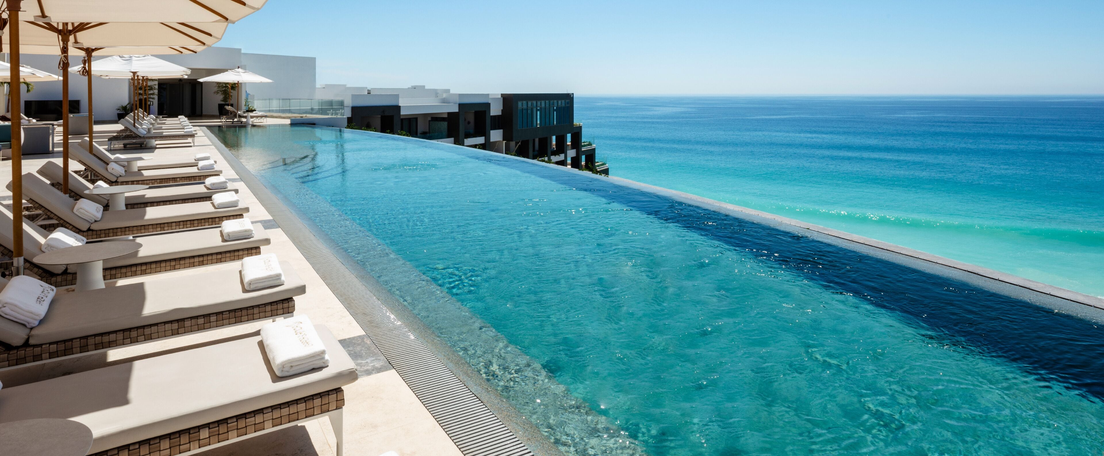 A poolside area with lounge chairs and umbrellas, overlooking a clear blue ocean.