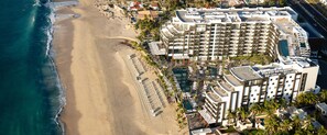 An aerial view of a beachfront hotel with multiple buildings, a sandy beach, and a pool area.