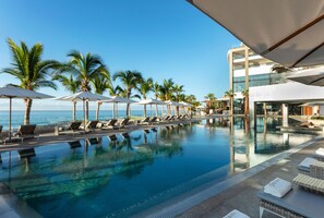 Ein Poolbereich mit Liegestühlen und Sonnenschirmen, Palmen und Blick auf das Meer.