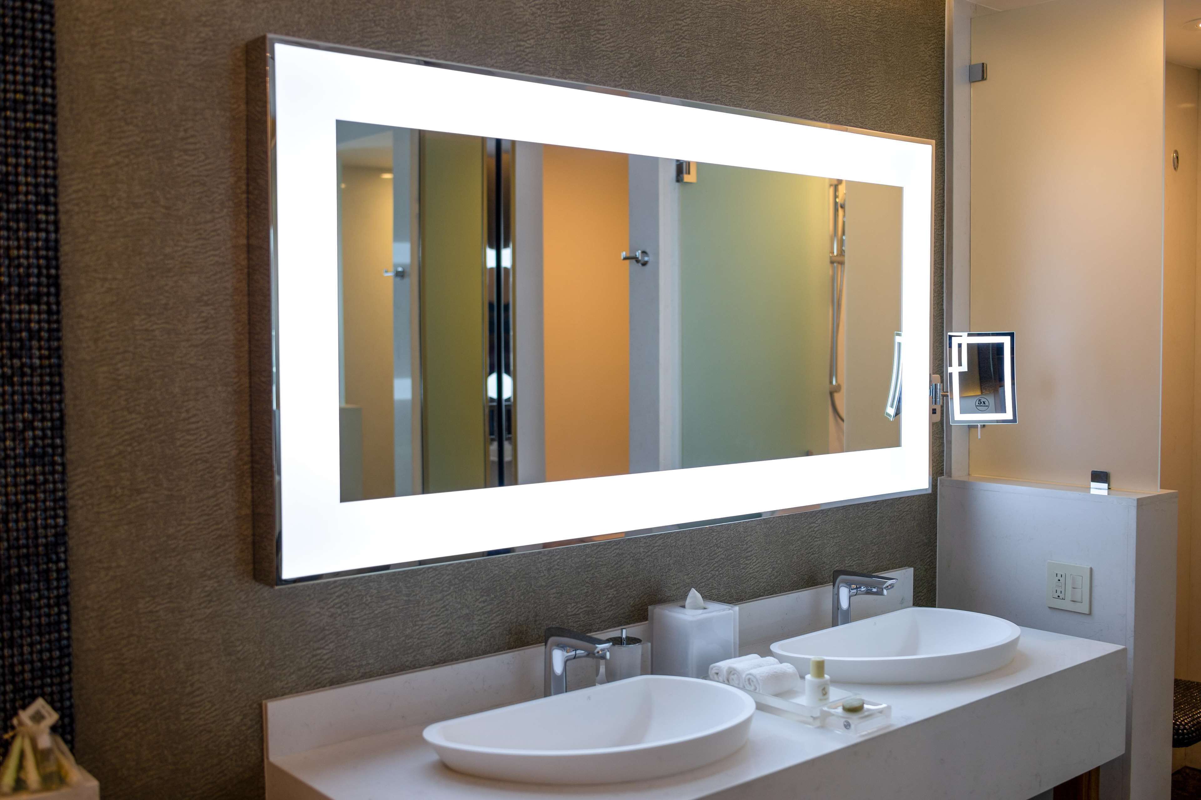 Un baño moderno con un espejo grande, dos lavamanos y una ducha.