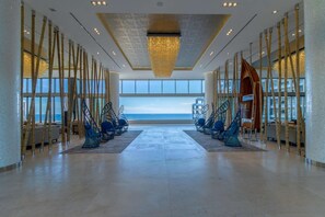 A spacious lobby with a large view of the sea, a modern chandelier, and bamboo columns.