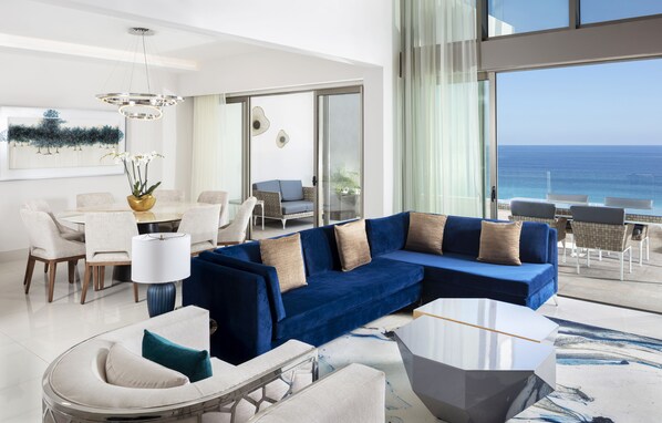 A modern living room with a blue sectional sofa, a round coffee table, and a dining area with a white table and chairs.