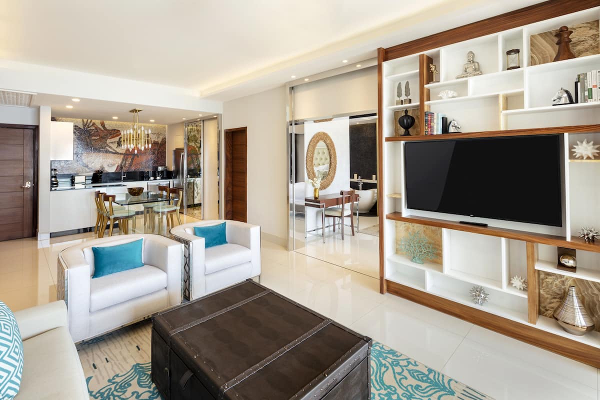 Ein modernes Wohnzimmer mit großem Fernseher, weißen Sofas, einem Couchtisch und einem Essbereich mit Glastisch und Stühlen.
