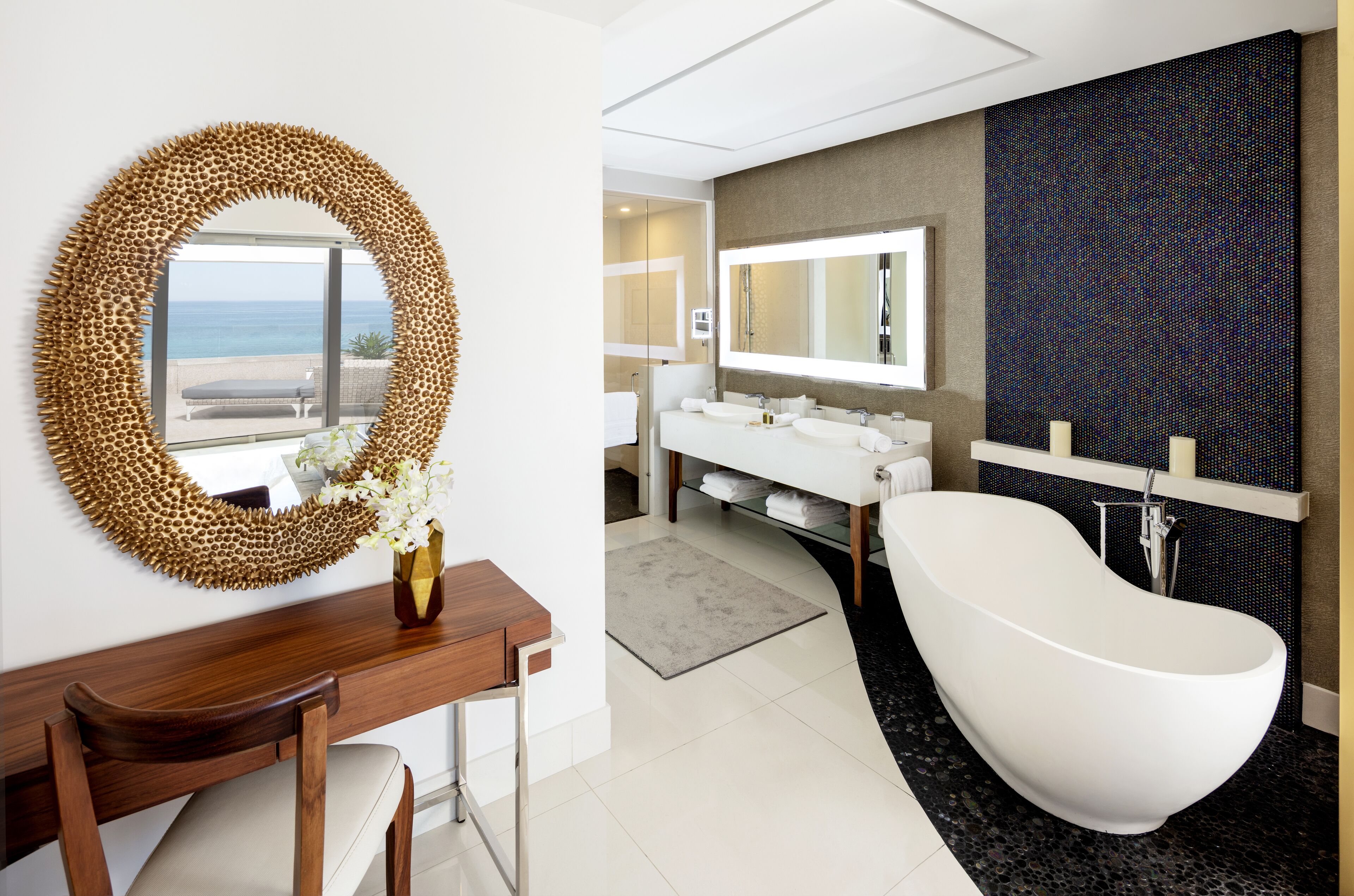 Un baño moderno con una bañera independiente, un espejo grande y vistas al océano.