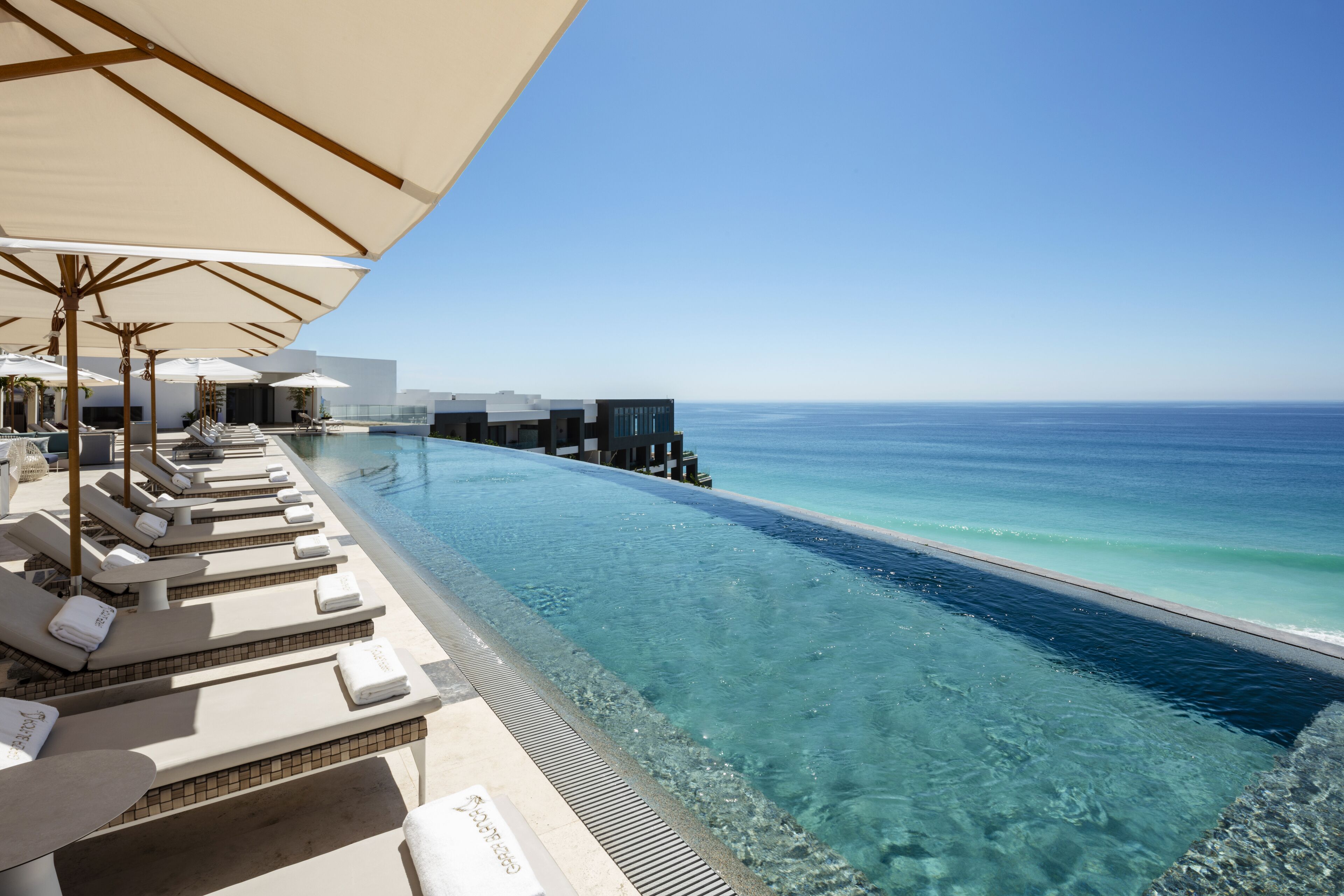 A infinity pool with clear water, lounge chairs, and umbrellas, overlooking the ocean.