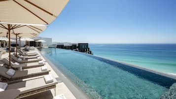 A infinity pool with clear water, lounge chairs, and umbrellas, overlooking the ocean.