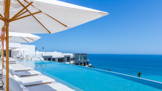 Un complexe hôtelier moderne doté d’une piscine donnant sur l’océan, de chaises longues et de parasols.