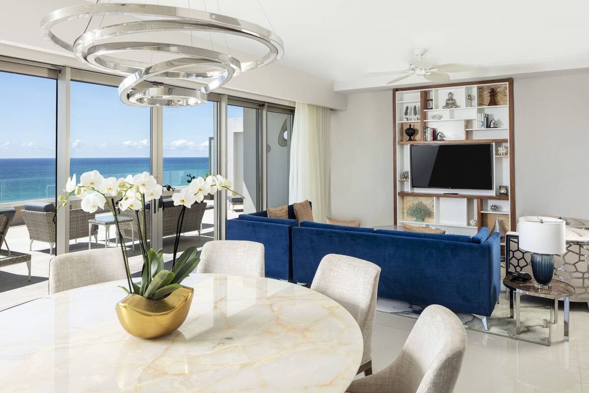 Ein modernes Wohnzimmer mit einem großen Fernseher, einem blauen Sofa und einem Essbereich mit einem Marmortisch und Orchideen.