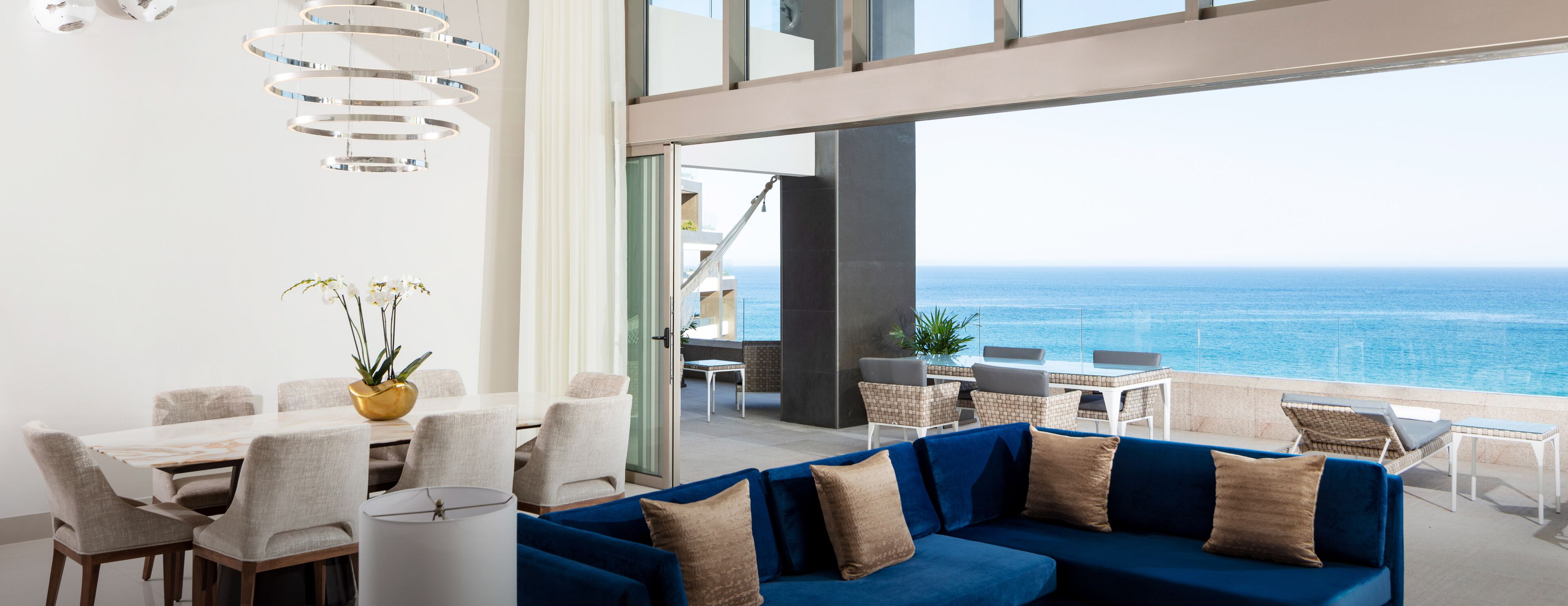 Decoração moderna com área de refeições, sofá azul e vista para o oceano.