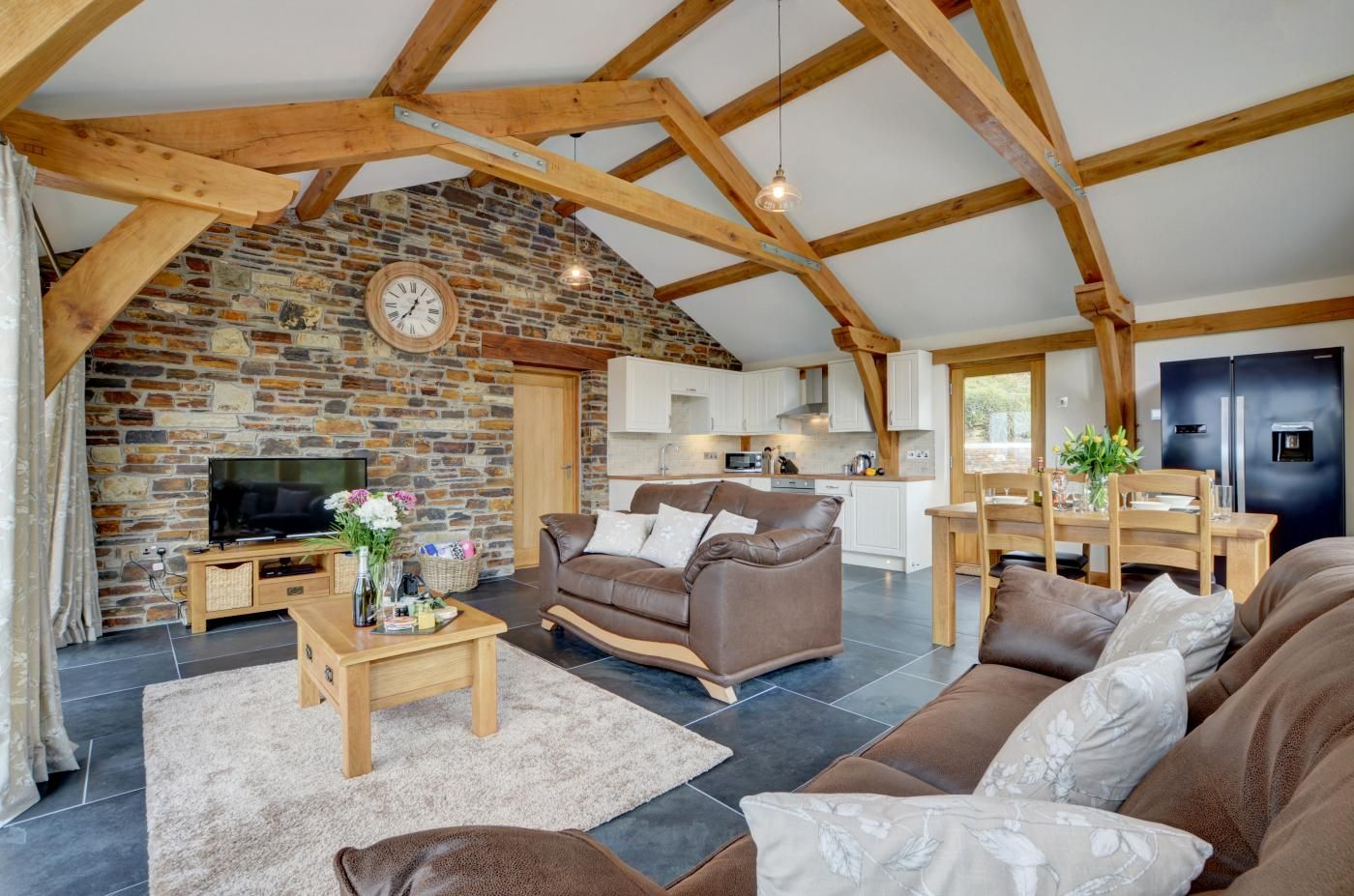 A rustic interior with exposed wooden beams, a stone fireplace, a modern kitchen, and a cozy living area with a sofa and coffee table.