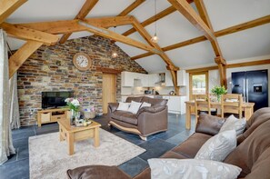 A rustic interior with exposed wooden beams, a stone fireplace, a modern kitchen, and a cozy living area with a sofa and coffee table.