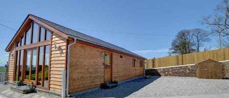 Una cabaña de madera con ventanas grandes, techo inclinado y camino de entrada de grava.