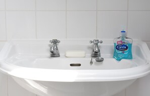 A white bathroom sink with two faucets, a soap dish, and a bottle of Carex Complete hand soap. - Stylish, comfortable apartment in  Leamington Spa (Royal Leamington Spa)