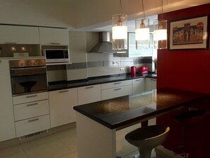 A modern kitchen with white cabinets, a black countertop, and a red accent wall.