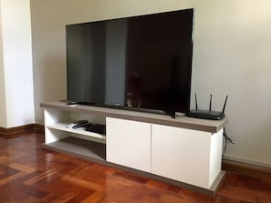 Ein Flachbildfernseher auf einer weißen Unterhaltungsanlage mit einer Holztischplatte, einer Fernbedienung und einem Kabelanschlussgerät.