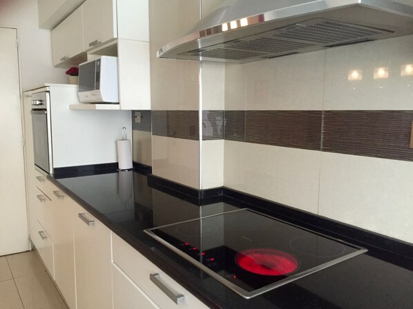 A modern kitchen with a black countertop, stainless steel range hood, and white cabinets.