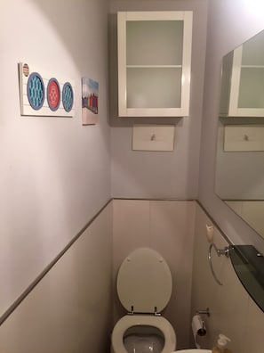 Ein Badezimmer mit Toilette, Waschbecken und Spiegel. An der Wand hängen drei Bilder in Rahmen.