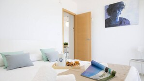 A hotel room with a bed, pillows, a tray with food and drinks, a magazine, and a painting on the wall. - Singular Stays Cullera Beach (Cullera)