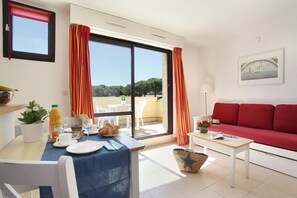 A living room with a red sofa, a dining table with breakfast items, and a view of the outdoors through a sliding door.