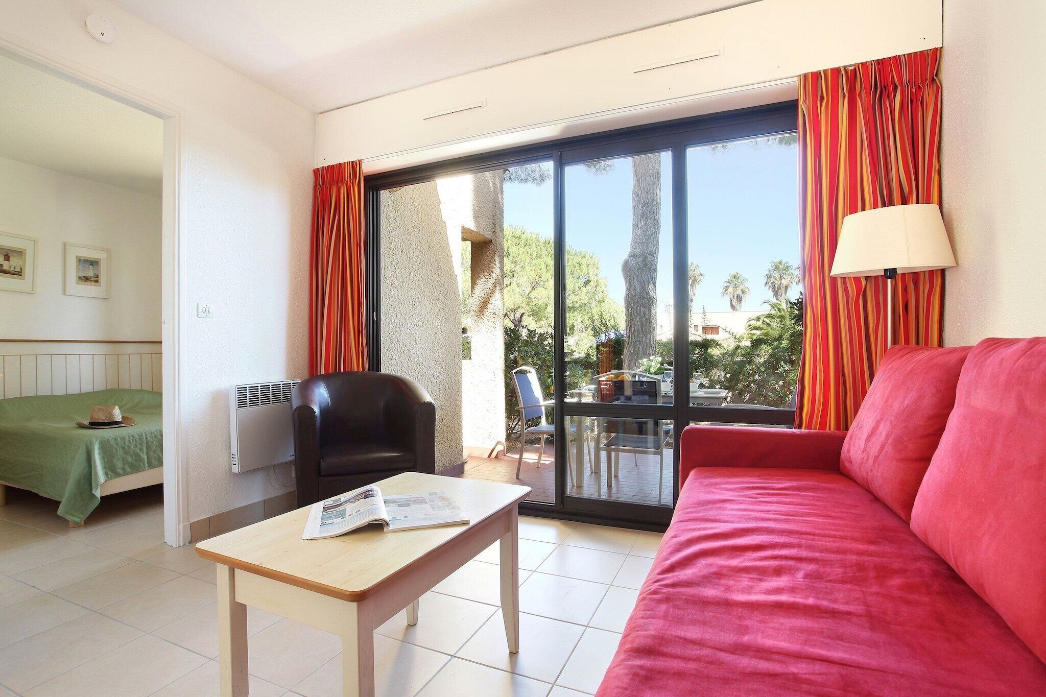 Ein Hotelzimmer mit Bett, Schreibtisch, Stuhl, einem roten Sofa und einer Glastür zum Außenbereich.
