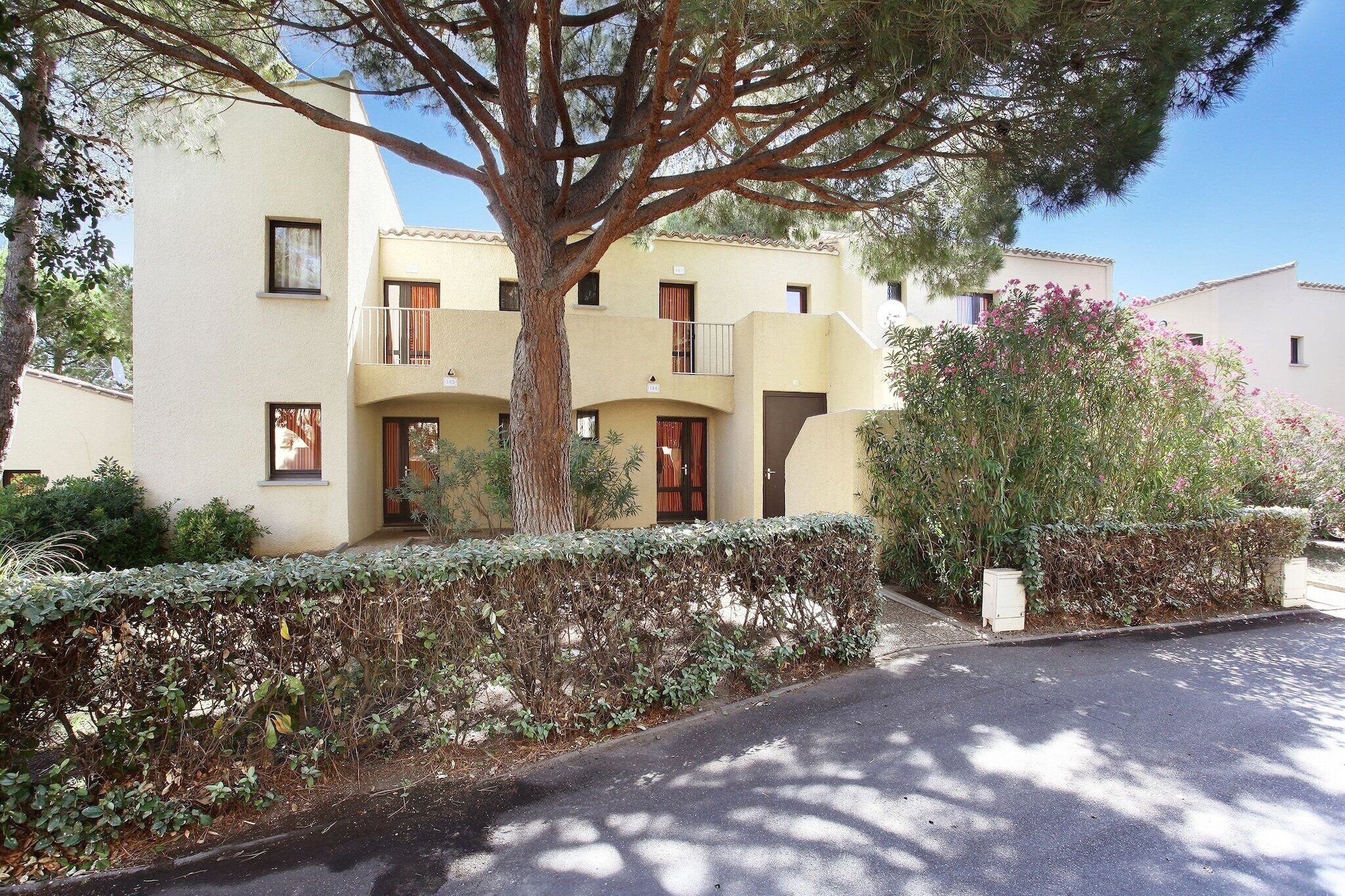 A residential building with a two-story structure, balconies, and a tree in the foreground.