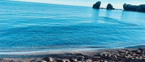 A beach with clear blue water and rocky formations in the distance.