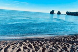 A beach with clear blue water and rocky formations in the distance. - Apartment in Saint-Loup amid Pine Trees (Agde)