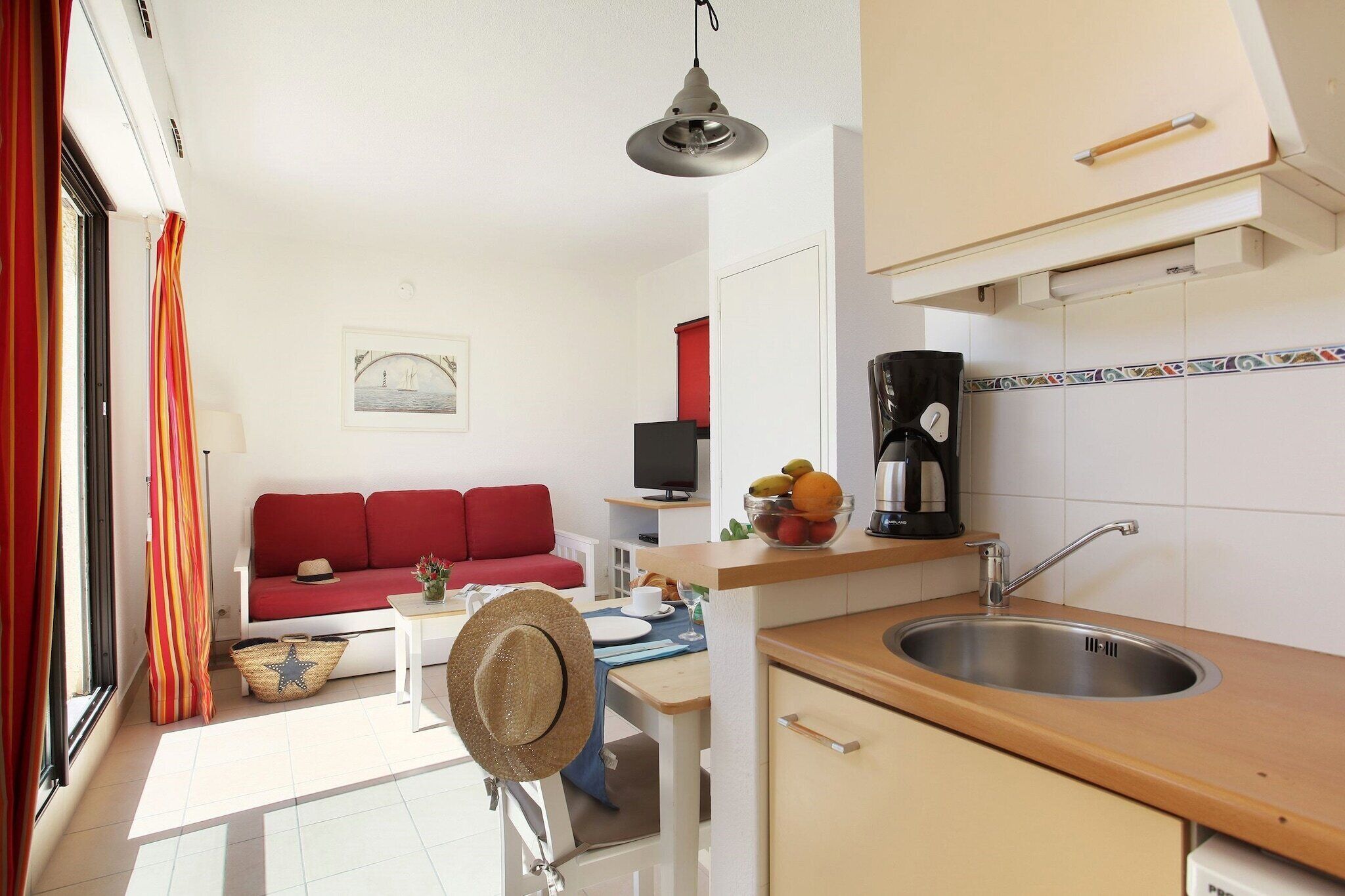 A compact kitchen with a sink, a coffee maker, and a dining area with a red sofa and a table set for two.
