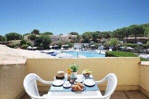 A dining table with breakfast items, overlooking a swimming pool with lounge chairs and umbrellas.