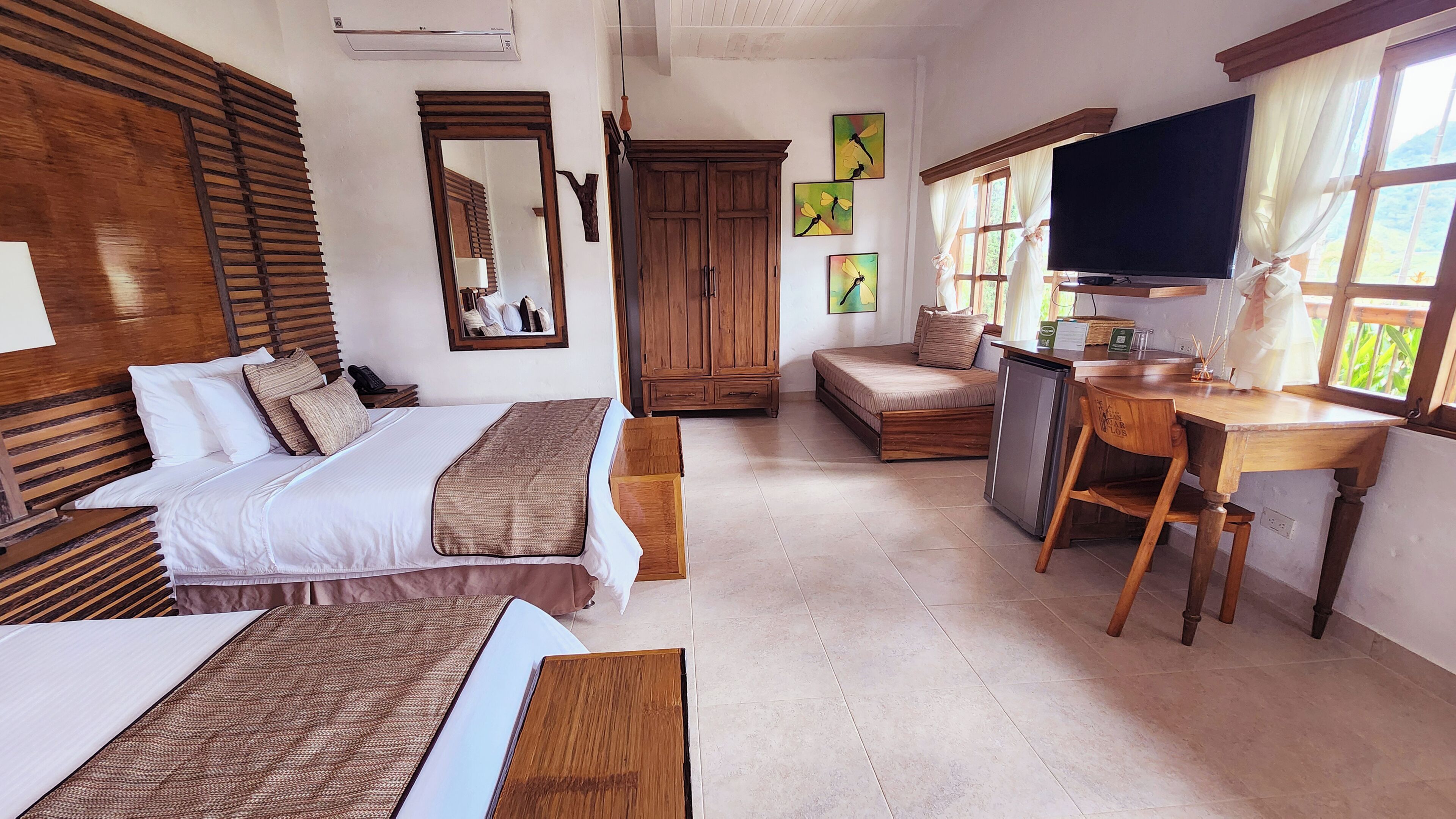 Quarto de hotel com duas camas, uma escrivaninha, televisão e guarda-roupa.