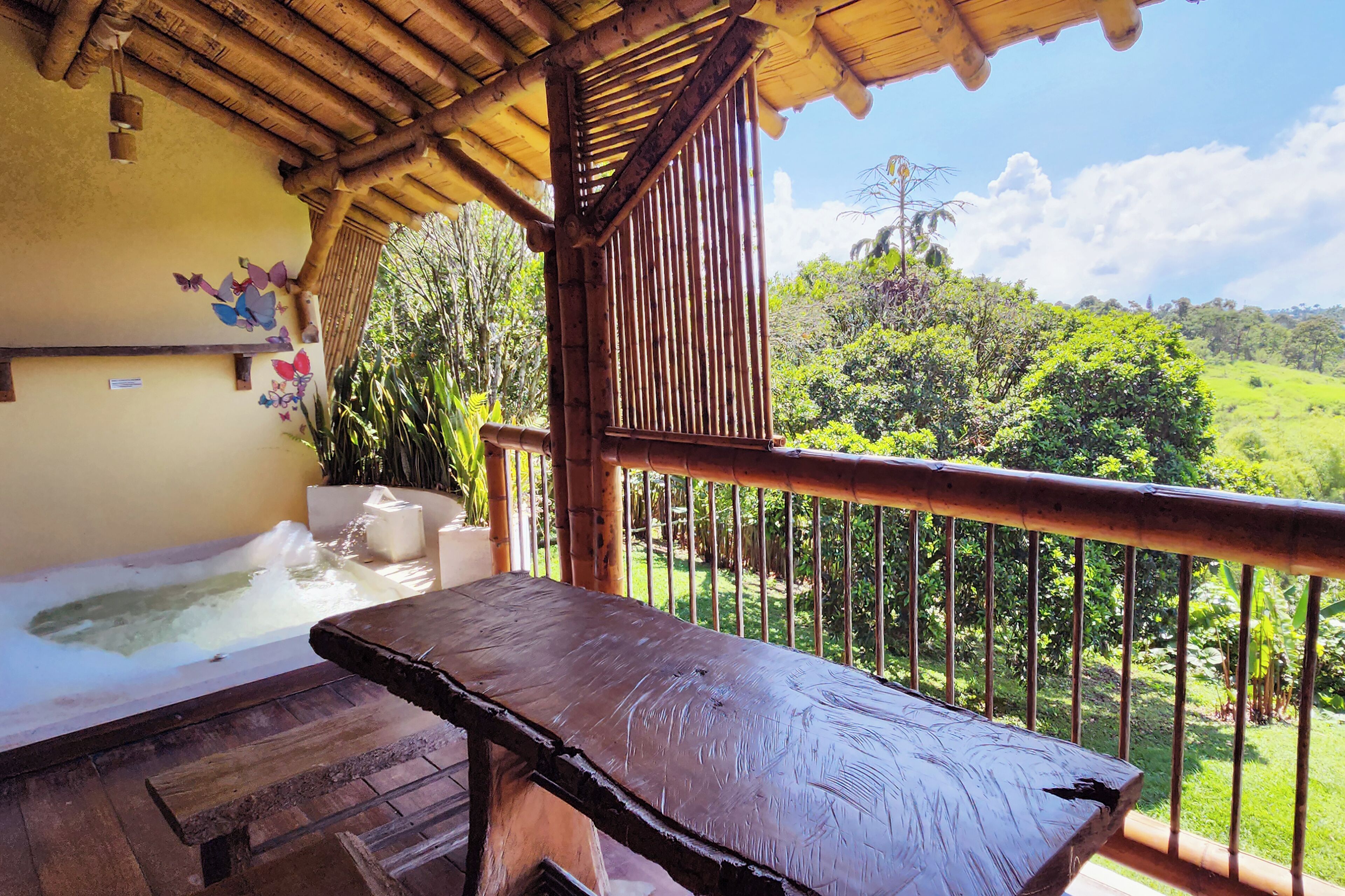 A wooden deck with a hot tub and a table, overlooking a lush green landscape.