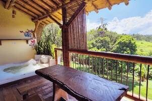 A wooden deck with a hot tub and a table, overlooking a lush green landscape.
