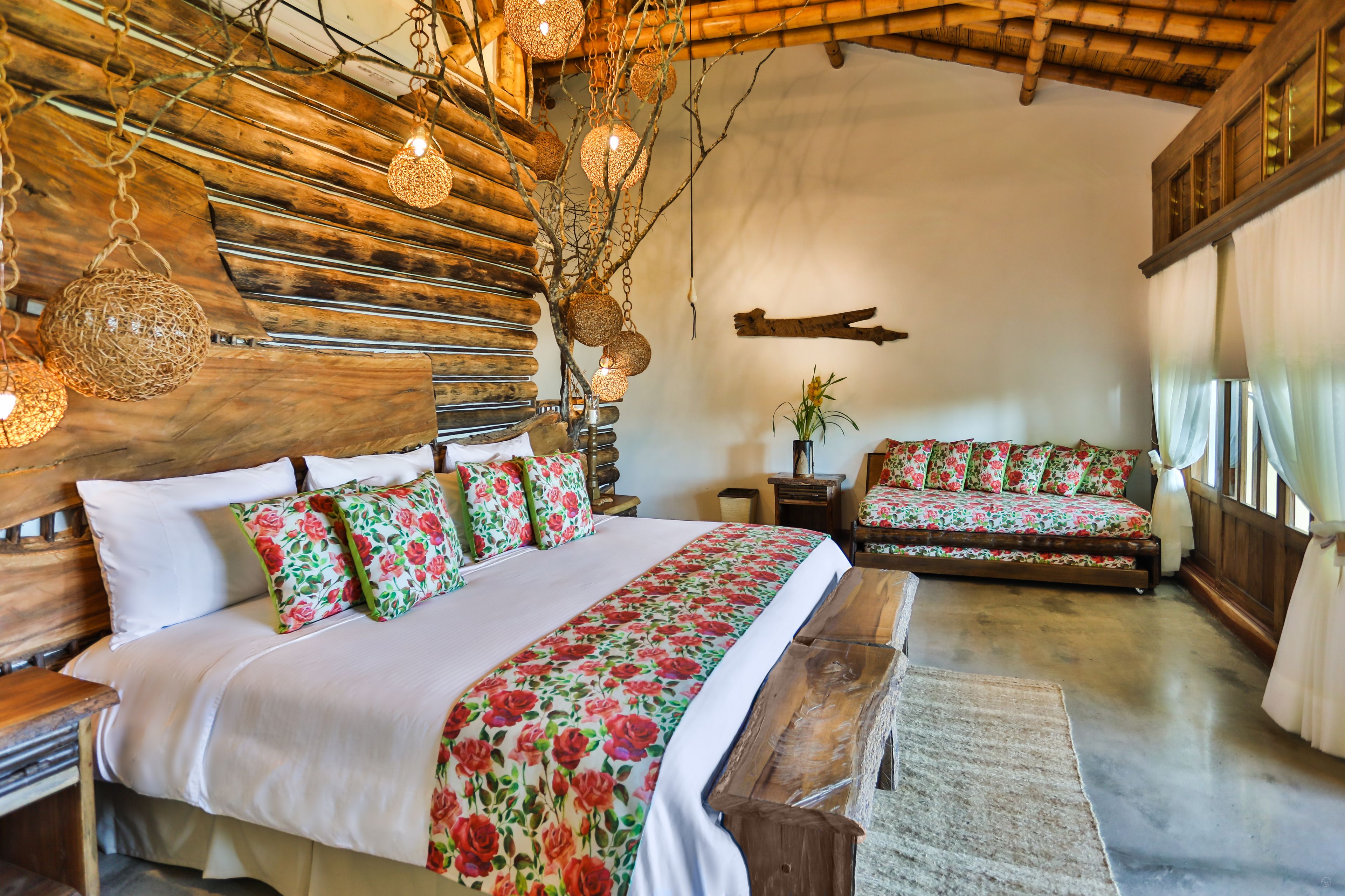A bedroom with a wooden headboard, a large bed with floral bedding, a bench, and a small table with a plant.