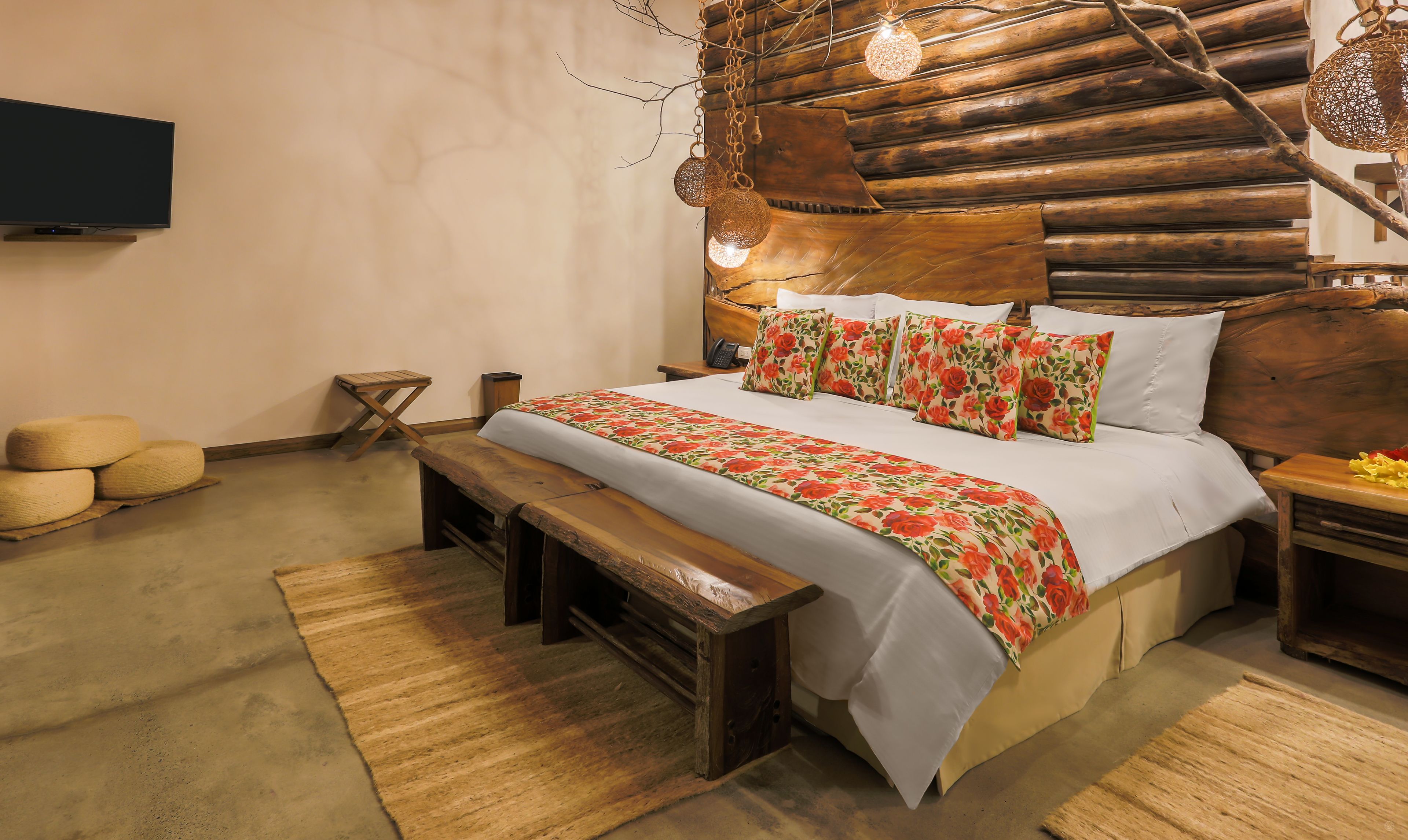 A rustic bedroom with a wooden headboard, a bed with floral bedding, a bench, and a television on the wall.