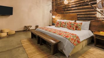 A rustic bedroom with a wooden headboard, a bed with floral bedding, a bench, and a television on the wall.