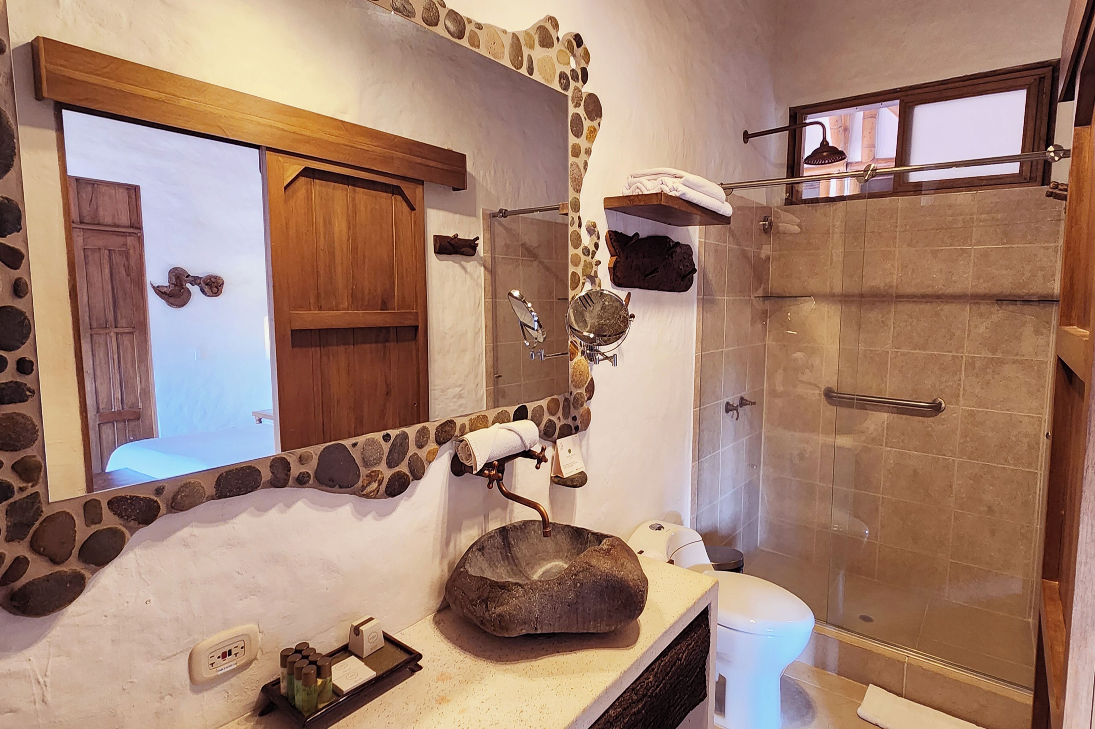 Une salle de bain avec un lavabo en pierre, une porte en bois, un porte-serviettes et un espace douche.
