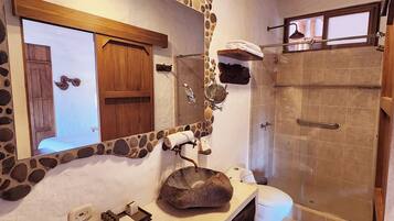 Une salle de bain avec un lavabo en pierre, une porte en bois, un porte-serviettes et un espace douche.