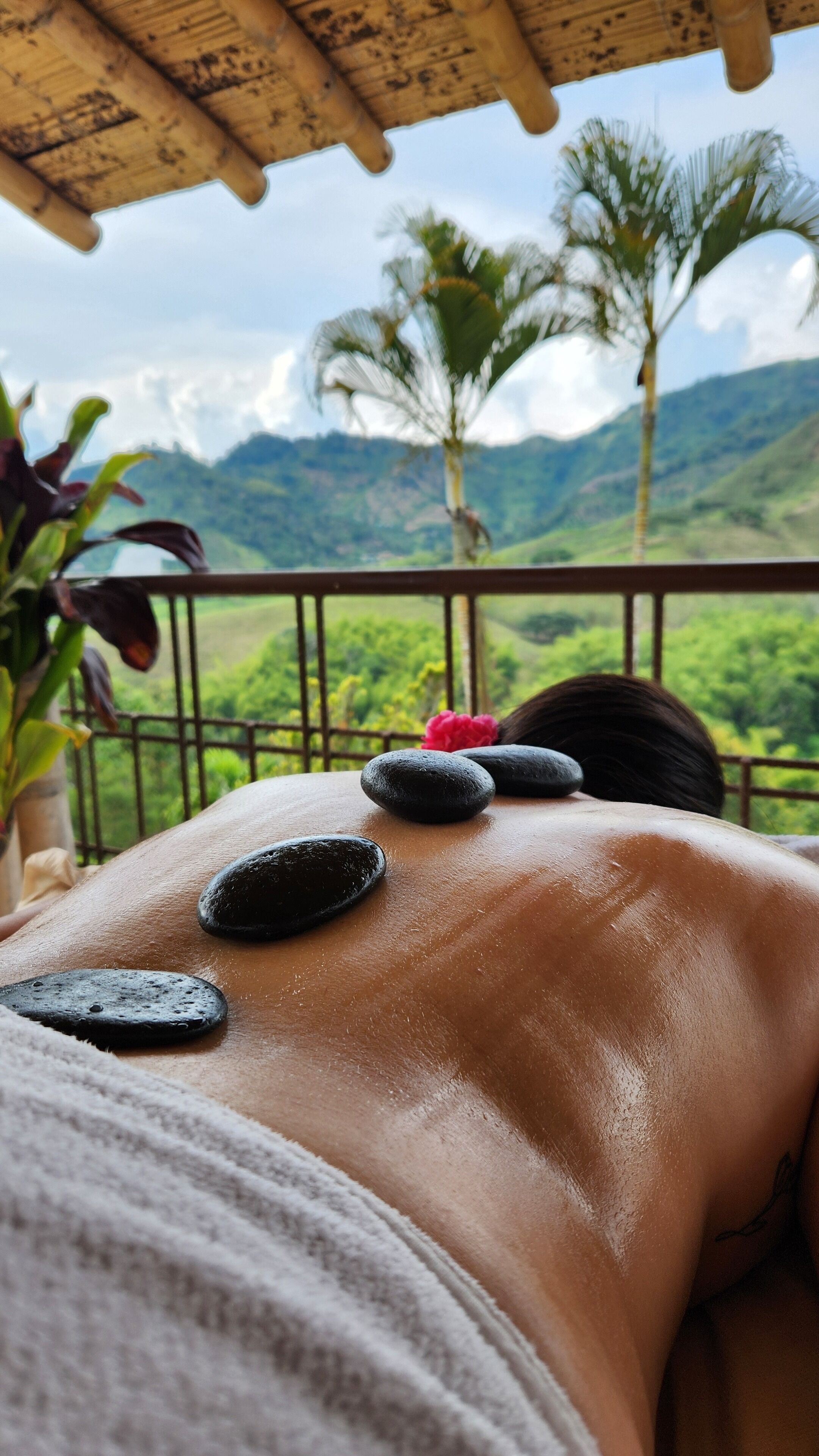 A person receiving a back massage with stones on their back, with a view of mountains and palm trees in the background.