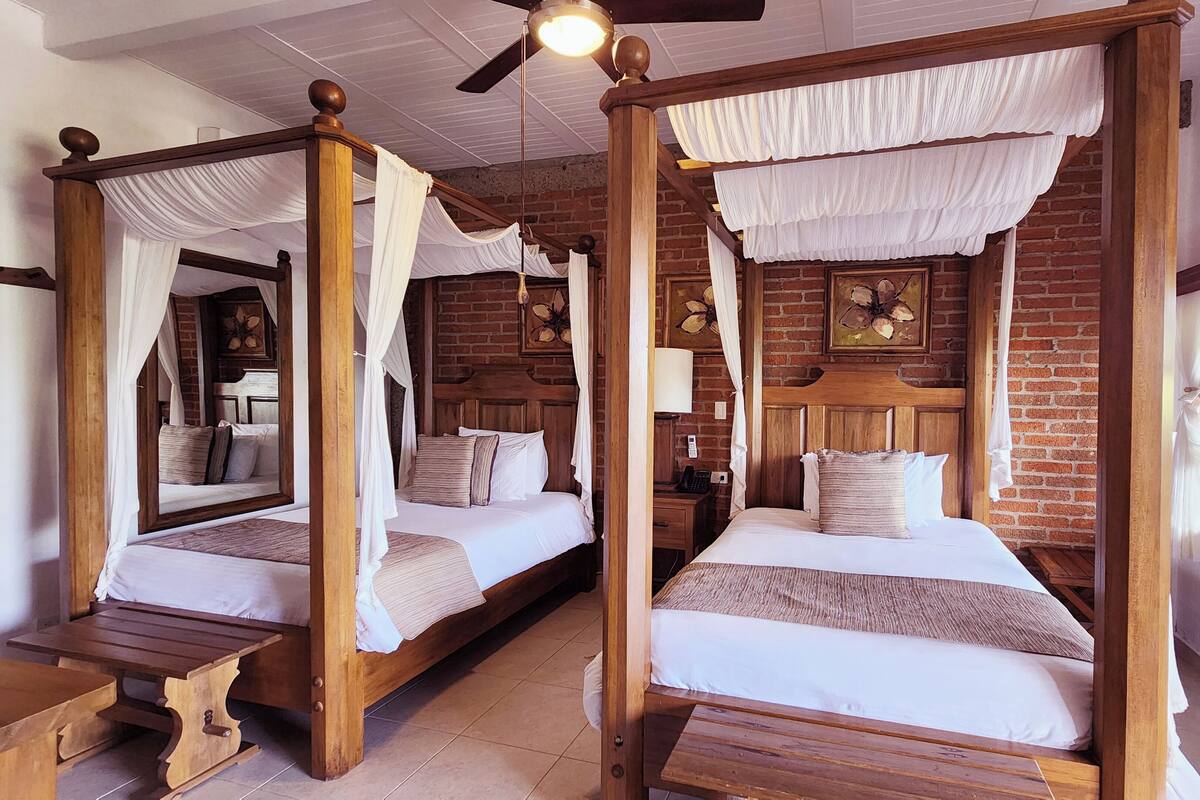 A room with two four-poster beds, wooden furniture, a brick wall, and a window with curtains.