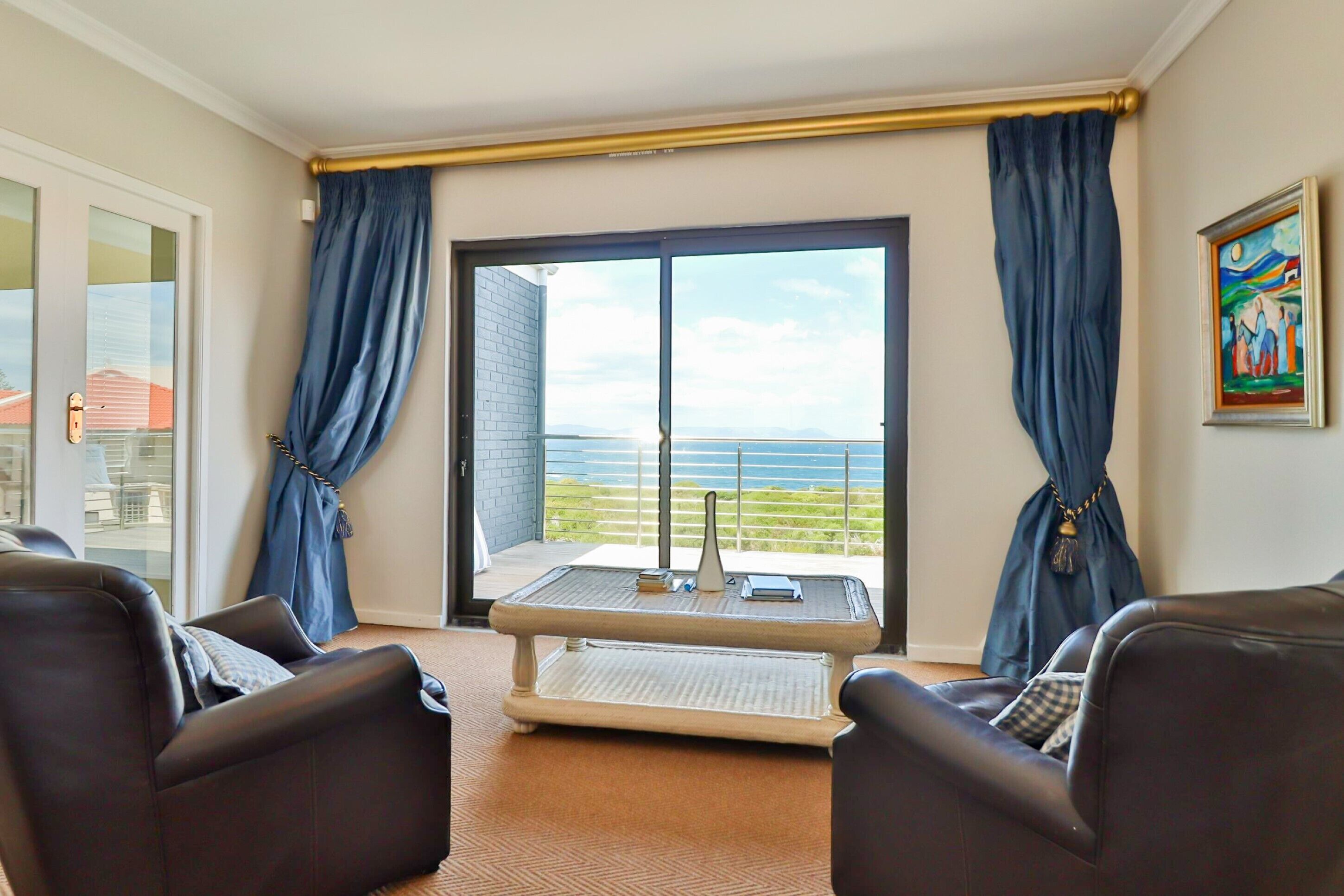 A balcony with a view of the sea, furnished with two leather chairs and a small table.