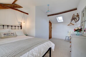 A bedroom with a bed, a dresser, a hanging light fixture, a skylight, and a wooden door.