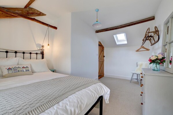 A bedroom with a bed, a dresser, a hanging light fixture, a skylight, and a wooden door.