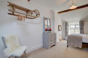 A bedroom with a bed, a dresser, a chair, a mirror, and a hanging rack.