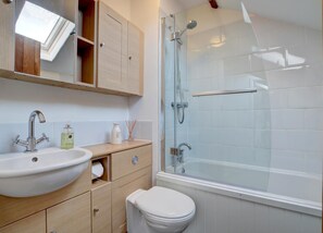 A bathroom with a sink, mirror, cabinet, toilet, and a glass-enclosed shower.