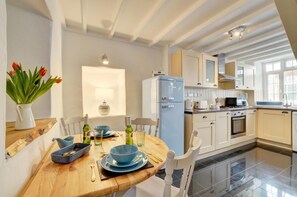 Una cocina moderna con una mesa de comedor para dos personas, un refrigerador y vistas del área de estar contigua.