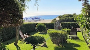 A well-maintained garden with a bench, a statue, and a view of the beach.